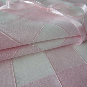 May include: Close-up of folded pink and white chequered fabric, possibly a tablecloth or napkins, tied with a matching pink ribbon. The fabric has a quilted appearance with stitched lines creating the chequered pattern.