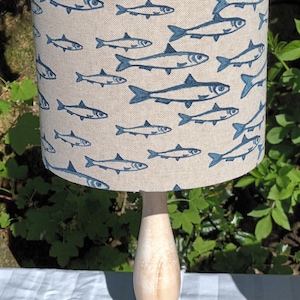 Puede incluir: Una base de lámpara blanca con una pantalla beige con un patrón de peces azules.