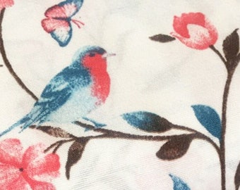 May include: White fabric with a repeating pattern of pink flowers, blue butterflies, and brown branches. A blue bird with a red breast is perched on a branch.