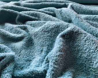May include: Close-up of a soft, blue, textured fabric. The fabric has a fluffy, towel-like texture.