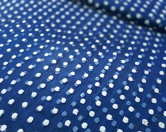May include: Blue fabric with a white polka dot pattern. The fabric has a crinkled texture.