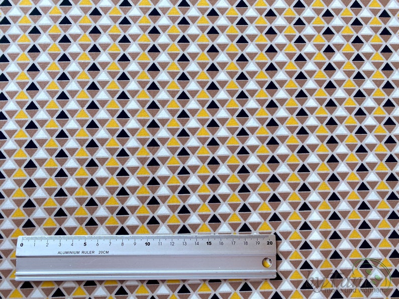 May include: A white fabric with a repeating pattern of small yellow, brown, and black triangles.