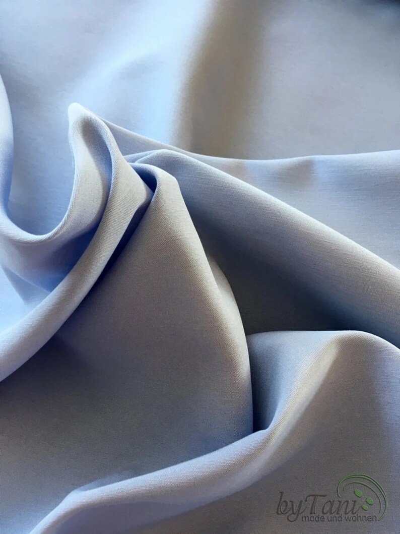 May include: Close-up of light blue fabric with soft folds and subtle shadows. The fabric appears smooth and possibly silky, with a gentle sheen. The overall effect is one of delicate texture and a calming color palette.