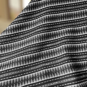 May include: Black and white fabric with a geometric pattern of triangles and lines. The fabric has a textured surface.