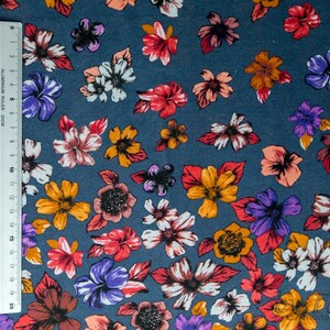 May include: A close-up of a blue fabric with a floral pattern. The flowers are in shades of red, orange, purple, and white. The fabric is perfect for crafting projects, quilting, or making clothing.