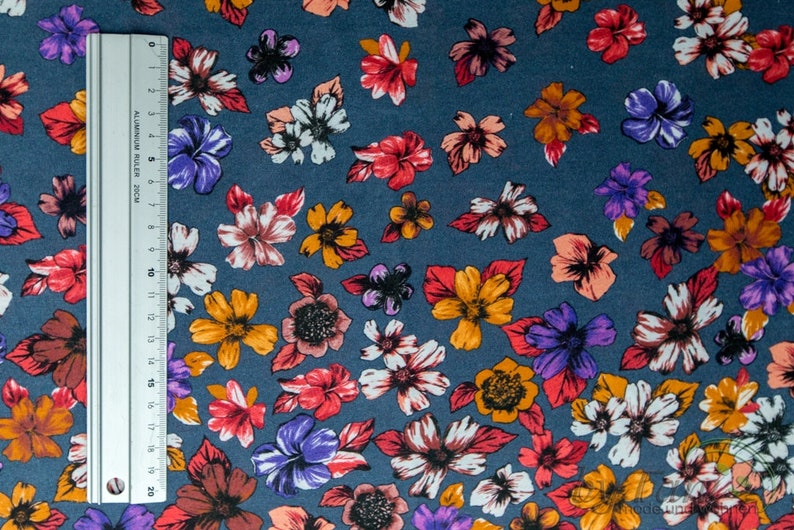 May include: A close-up of a blue fabric with a floral pattern. The flowers are in shades of red, orange, purple, and white. The fabric is perfect for crafting projects, quilting, or making clothing.