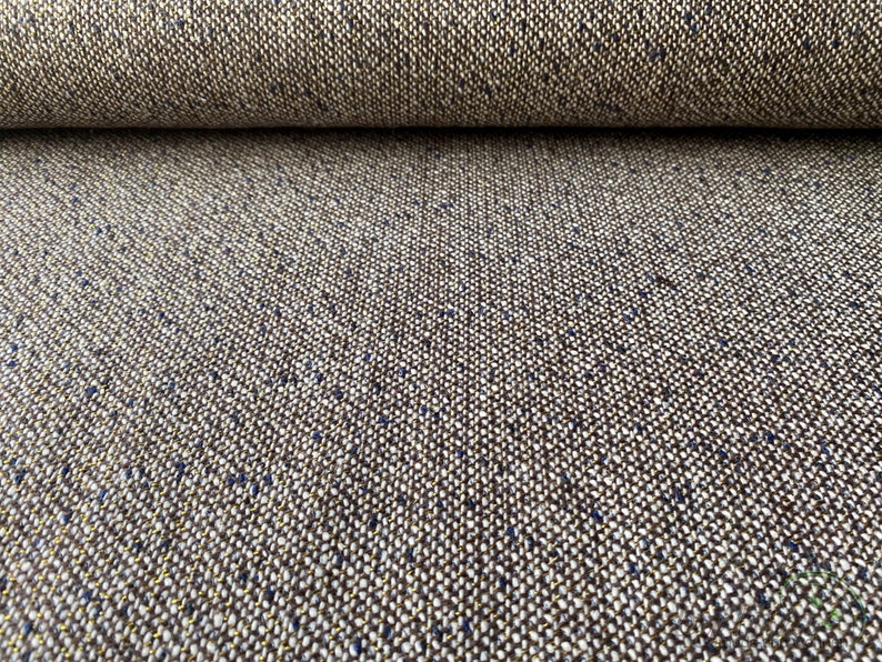 Op de afbeelding: Close-up van een bruine tweed stof met een subtiele glans van blauwe en gouden draad. De stof heeft een textuur geweven patroon.