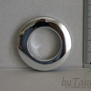 May include: A silver metal curtain ring with a 1-inch inner diameter. The ring is shown next to a ruler for size reference.
