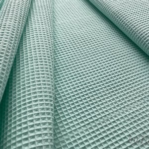 Puede incluir: Primer plano de una tela de tejido de gofre azul claro. La tela está doblada y muestra la textura del tejido.