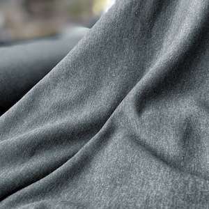 May include: Close-up of a dark gray fabric with a textured surface. The fabric is folded and draped, showing its soft and drapey texture.