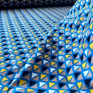 以下が含まれることがあります： 白、黄、黒の三角形が幾何学的に並んだ青い布地