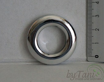May include: A shiny, silver-colored grommet with a smooth, rounded design. The grommet is circular with a central opening. A ruler is placed next to the grommet, showing measurements in inches. The grommet is likely used for curtains or other fabric projects.