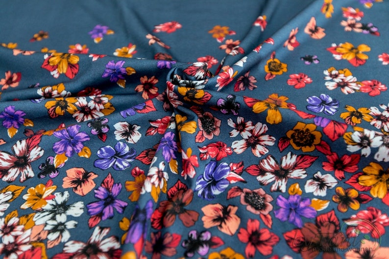 May include: A teal blue fabric with a floral print. The flowers are in shades of red, orange, purple, and white.