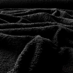 May include: Close-up of a black, soft, and textured fabric. The fabric is folded and draped, creating a wavy pattern.