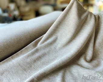 May include: Close-up of a beige ribbed knit fabric. The fabric is soft and has a subtle texture. It is perfect for sewing clothing or accessories.