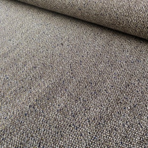 Op de afbeelding: Close-up van een bruine tweed stof met een subtiele blauwe vlek. De stof heeft een textuurweving en een zacht, natuurlijk gevoel.