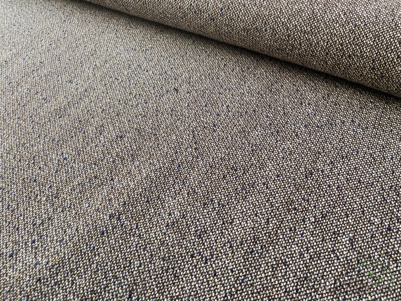 Op de afbeelding: Close-up van een bruine tweed stof met een subtiele blauwe vlek. De stof heeft een textuurweving en een zacht, natuurlijk gevoel.