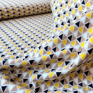 May include: A white fabric with a geometric pattern of small yellow, brown, and black triangles. The fabric is folded and draped, showing the pattern.