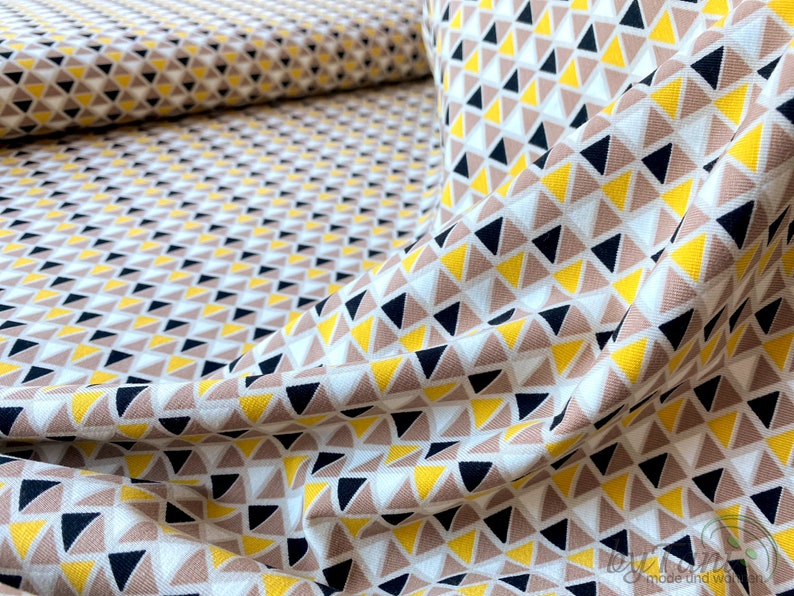 May include: A white fabric with a geometric pattern of small yellow, brown, and black triangles. The fabric is folded and draped, showing the pattern.