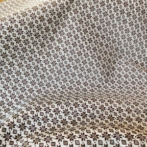 May include: White fabric with a brown snowflake pattern. The fabric is folded and has a textured surface.