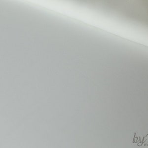 May include: A close-up of a white fabric with a subtle texture. The fabric is folded in half, creating a diagonal line across the image. The text "byTani - mode und wohnen" is visible in the lower right corner.