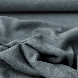 May include: Close-up of a soft, gray fabric with a textured surface. The fabric is folded and draped, showing its drapability and texture.