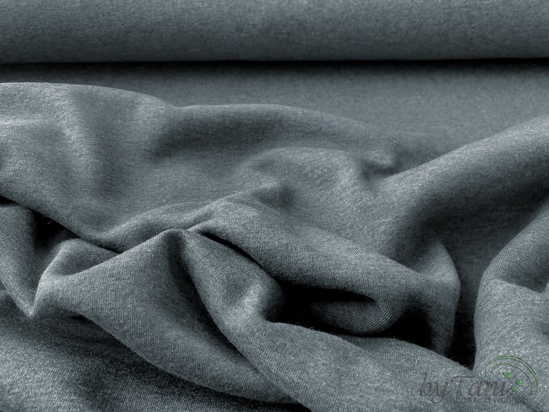May include: Close-up of a soft, gray fabric with a textured surface. The fabric is folded and draped, showing its drapability and texture.