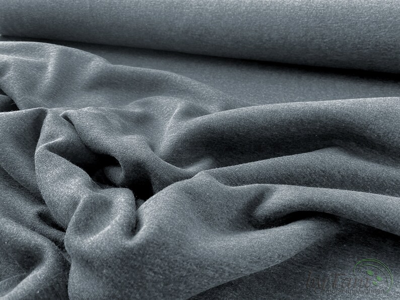 May include: A close-up of a soft, gray fabric with a textured surface. The fabric is folded and draped, showing its texture and drape.