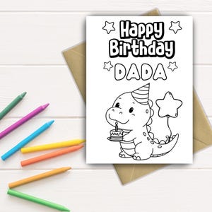 Op de afbeelding: Een zwart-wit verjaardagskaart met de tekst "Happy Birthday DADA" en een cartoon dinosaurus met een taart. De kaart ligt op een bruine envelop, met kleurpotloden verspreid.