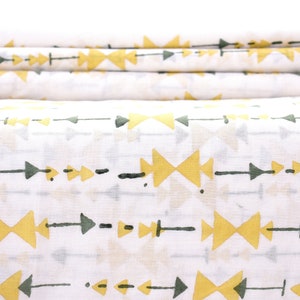 May include: White fabric with a repeating pattern of yellow arrows and green triangles. The fabric is folded in thirds.