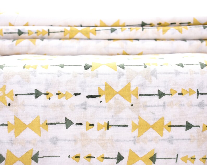 May include: White fabric with a repeating pattern of yellow arrows and green triangles. The fabric is folded in thirds.
