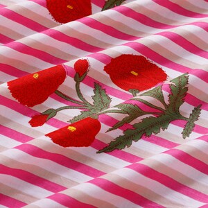 Op de afbeelding: Roze en witte gestreepte stof met een rode bloemenprint. De stof heeft een herhalend patroon van rode bloemen met groene bladeren.
