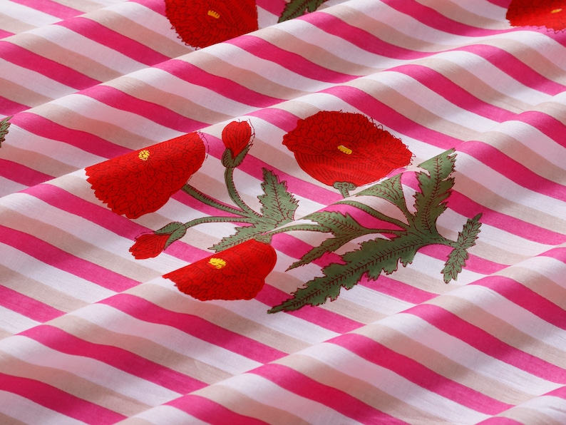 Op de afbeelding: Roze en witte gestreepte stof met een rode bloemenprint. De stof heeft een herhalend patroon van rode bloemen met groene bladeren.