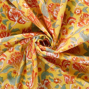 Puede incluir: Tela amarilla con un patr&oacute;n floral en tonos naranja, rojo y verde. La tela est&aacute; doblada y retorcida, creando un efecto de remolino.