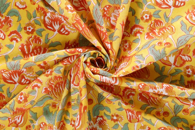 Puede incluir: Tela amarilla con un patr&oacute;n floral en tonos naranja, rojo y verde. La tela est&aacute; doblada y retorcida, creando un efecto de remolino.