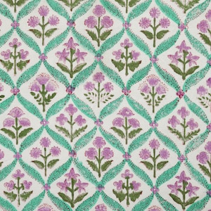 May include: A white fabric with a repeating pattern of pink and green flowers. The flowers are arranged in a grid pattern and are surrounded by a green vine.