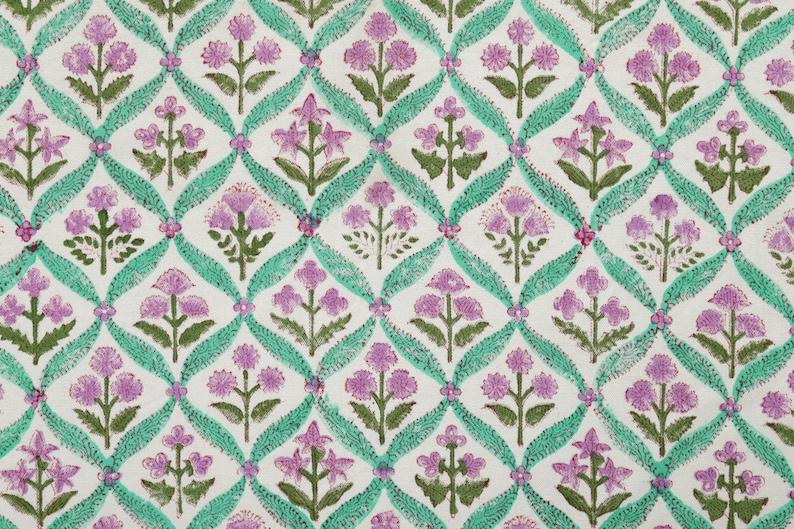 May include: A white fabric with a repeating pattern of pink and green flowers. The flowers are arranged in a grid pattern and are surrounded by a green vine.