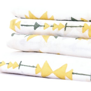May include: A stack of four white fabric squares with a geometric pattern of yellow triangles and green lines. The fabric is folded neatly and the pattern is visible on each square.