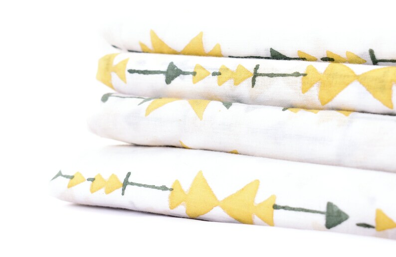 May include: A stack of four white fabric squares with a geometric pattern of yellow triangles and green lines. The fabric is folded neatly and the pattern is visible on each square.