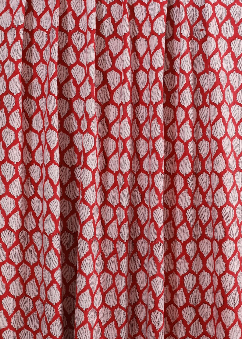 May include: Red fabric with a white leaf pattern. The leaves are arranged in a repeating pattern.