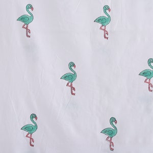 May include: White fabric with a repeating pattern of green flamingos. The flamingos are outlined in black and have pink legs.