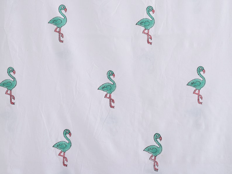 May include: White fabric with a repeating pattern of green flamingos. The flamingos are outlined in black and have pink legs.