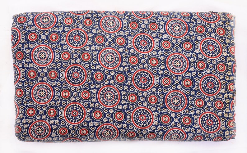 Op de afbeelding: Blauwe stof met een herhalend patroon van rode en witte cirkels met ingewikkelde ontwerpen erin. De stof heeft een traditionele Indiase stijl.