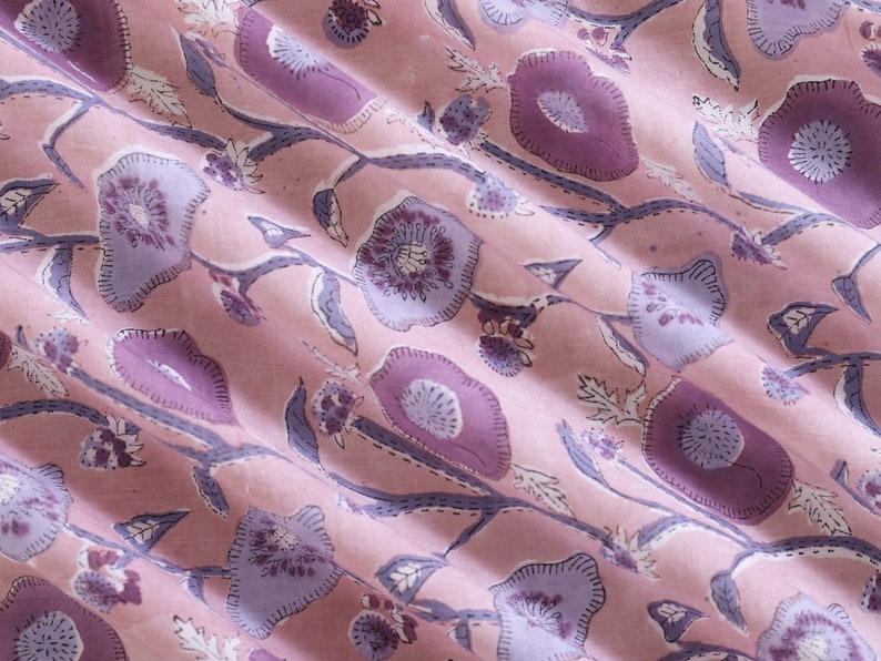 May include: Pink fabric with a floral pattern in shades of purple and white. The fabric has a subtle sheen and a soft texture.