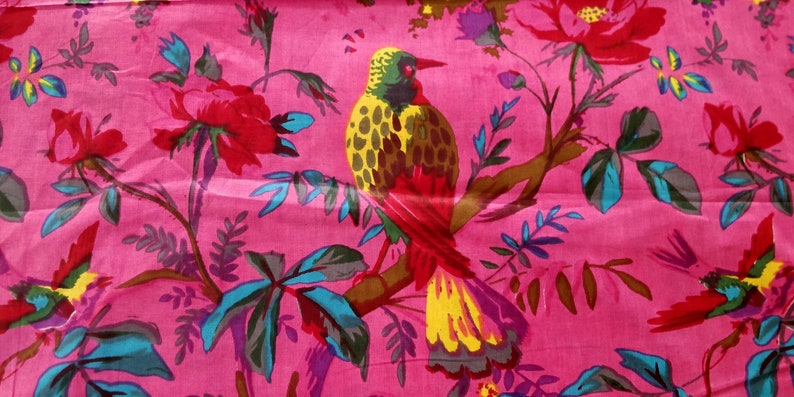 May include: A pink fabric with a repeating pattern of yellow, red, and blue birds perched on branches with pink and green flowers.