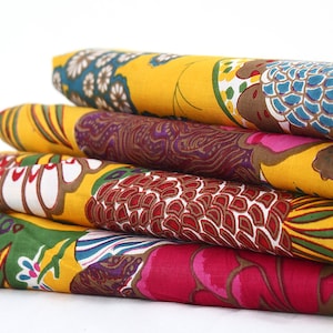 May include: A stack of four yellow fabric squares with colorful floral patterns. The fabric is folded and stacked, with the top layer showing a blue and brown floral design.