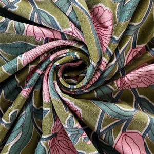 Pode incluir: Um tecido de veludo macio com um padr&atilde;o floral repetitivo de grandes flores cor-de-rosa, folhas verde-azulado e caules verde-escuros sobre um fundo verde-azeitona. O tecido est&aacute; reunido numa espiral central, real&ccedil;ando a sua textura.