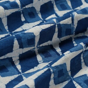 K&ouml;nnte beinhalten: Blauer und wei&szlig;er Stoff mit einem geometrischen Muster aus Quadraten. Der Stoff ist gefaltet und hat eine weiche, strukturierte Haptik.