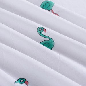 May include: White fabric with a green flamingo print. The flamingo is facing right and has a pink beak.