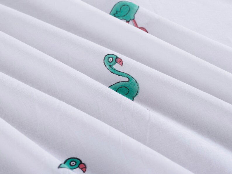 May include: White fabric with a green flamingo print. The flamingo is facing right and has a pink beak.